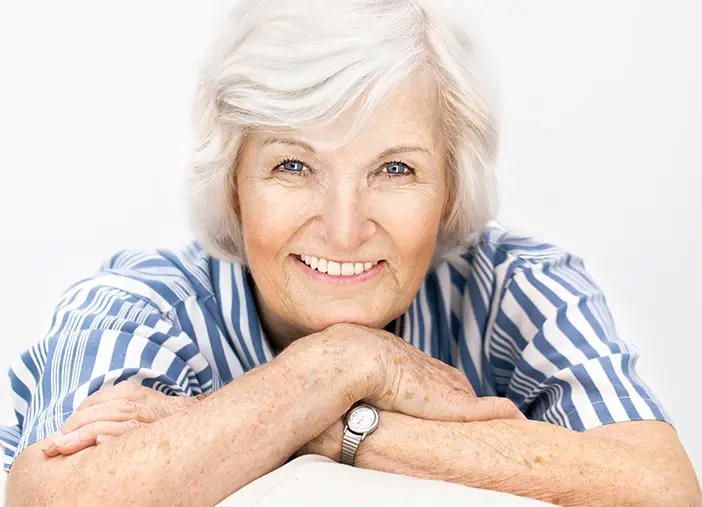 Seniorin mit weißen Haaren und blau-weiß gestreifter Bluse lächelt in die Kamera